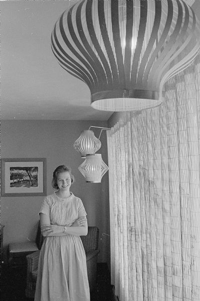 One of a series of photographs depicting ways U.W. graduate students have made their small apartments more attractive and livable. Shown is Marion Brown standing next to the bamboo draperies she and her husband painted white, then decorated with a watercolor mural. There are also lanterns made from bamboo place mats, coat hangers and construction paper.
