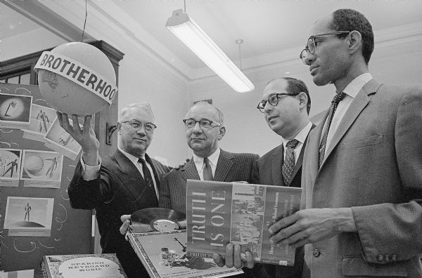 The Dane County National Association for the Advancement of Colored People (NAACP) Brotherhood Week display, including books, recordings and other materials, is set up at the Madison Central Library, 206 N. Carroll Street. Shown observing the display are, (L-R): Harold K. Hill and Attorney Maurice Pasch, co-chairman of the Brotherhood Week observance; Bernard Schwab, Madison Public Library Director; and Lloyd Barbee, NAACP member.