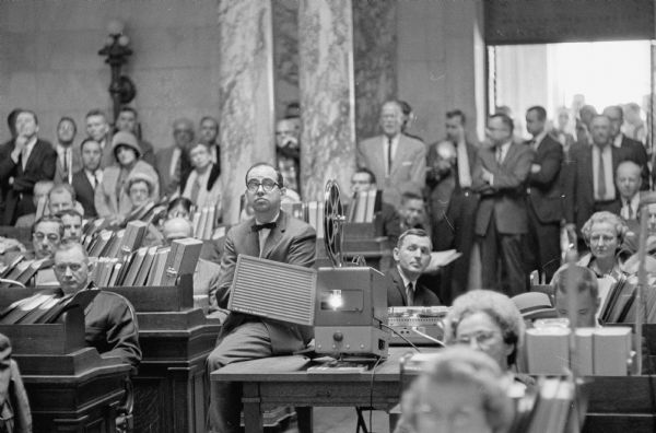 Public hearing on the proposed abolition of the House Un-American Activities committee at the Wisconsin State Capitol. All eyes are watching the movie "Operation Abolition" in the Wisconsin Assembly chamber at the beginning of the hearing. The projectionist is Edward Friend, Milwaukee, an official of the Nordberg Manufacturing Co. which made the film available.
