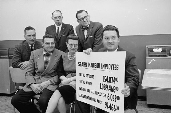 Five employees of Sears, Roebuck, and Company who have a stake in the company's profit-sharing plan. Controller, R. L. Roidt holds up a graphic illustration of the Madison employees' stake in the company. Looking on are Lester Daley and Ruth Staebler in front. In back, left to right, are Tony Breitenbach, A. J. Selje, and Stanley Hagen.