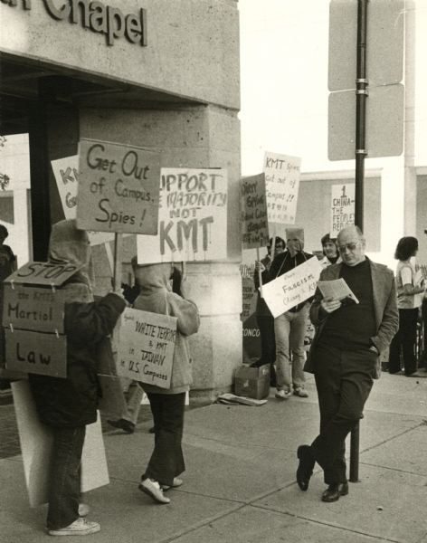 Students protesting the Kuomintang's authoritarian control of Taiwan on Library Mall at the Calvary Lutheran Chapel. In the foreground a man is leaning against a street sign pole reading.