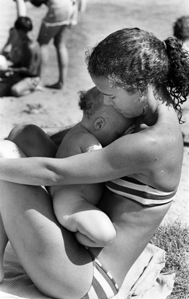 A mother cuddling her baby in her lap while sitting on a blanket at B.B. Clarke Beach.