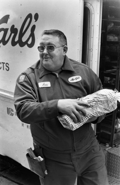 A Mrs. Karl's delivery man holding a loaf of bread near the open door of a delivery truck.