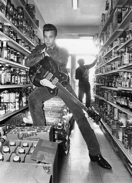 Dan "Ernie" Conner with his guitar in the aisle of a supermarket.