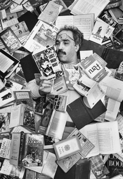 Overhead view of playwright Joel Gersmann lying on his back covered in a pile of books reading "Lost Highway."