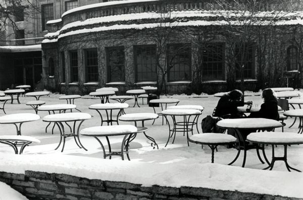 Two students sharing a bottle of wine at a table on the snowy terrace of the Memorial Union.