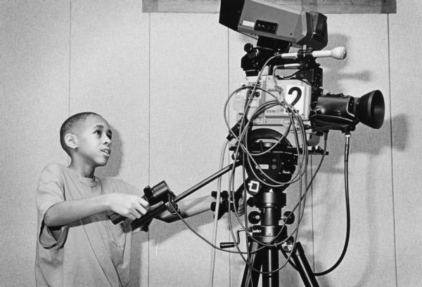 A young boy learning how to operate a television camera.