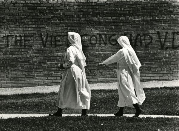 Two nuns walking past a graffitied wall on the University of Wisconsin campus.