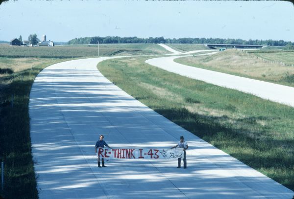 Two men holding a banner that reads: "Re-think I-43" in protest of the newly built highway. The highway runs from Green Bay to Beloit by way of Milwaukee.