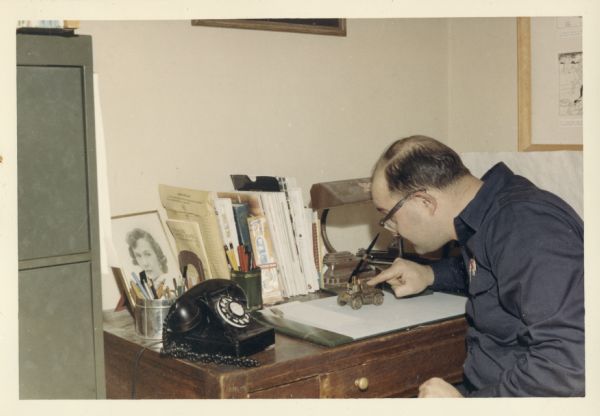 Gene Coffman, founder of Gratco Corporation, at his home office desk, 414 Clemons Ave., looking down at a small toy model.