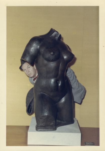 Sid Boyum playfully poking his head out from behind a sculpture of a woman's torso.