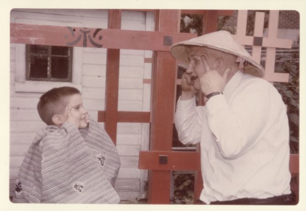 Eric Coffman and Sid Boyum making slanted-eye gestures at each other in Sid's backyard at 237 Waubesa Street. Eric is wearing a Kimono and Sid is wearing a conical straw hat.