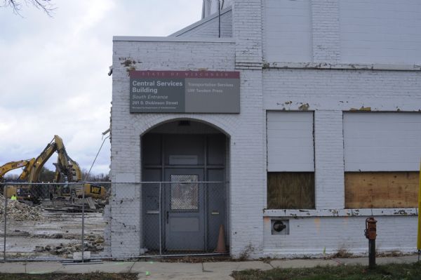 Front entrance to the State of Wisconsin's Central Services Building, located at 201 S. Dickinson Street. The building contained Transportation Services and the UW Tandem Press. The building is being torn down in preparation for building a new storage facility, the State Archives Preservation Facility (SAPF). In the background on the left are men standing by two Caterpillar 349E Hydraulic Excavators.