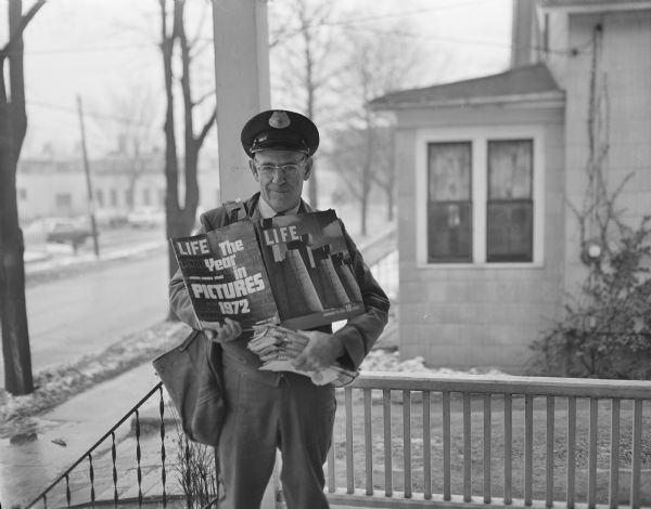 Portrait of the postal carrier Carl Wagner on the porch of Sid's house, displaying a <i>Life</i> magazine in his arms, and holding a stack of mail. 