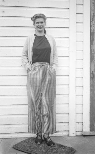 Bernice Boyum Bergner, Sid Boyum's sister, standing against the side of a clapboard building near a door.