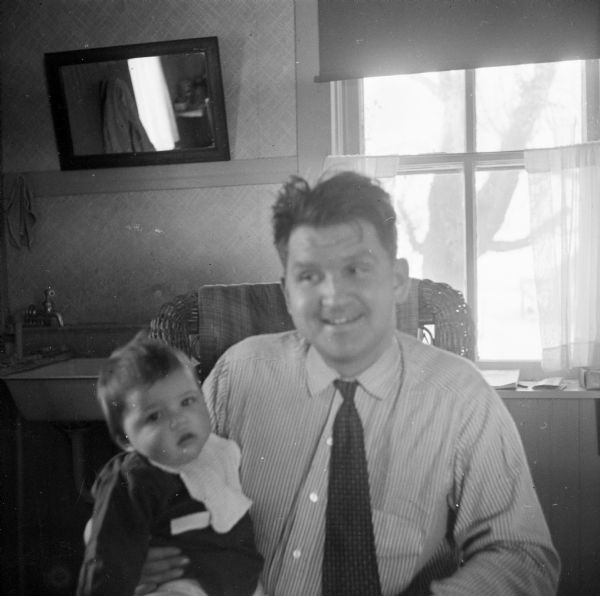 Portrait of Sid sitting in a chair with his son, Steve, on his lap. Behind them is a sink near a window.
