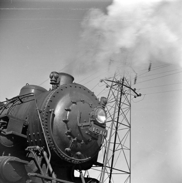 Right side view of the front of a steam locomotive. In the background is a high voltage power pole.