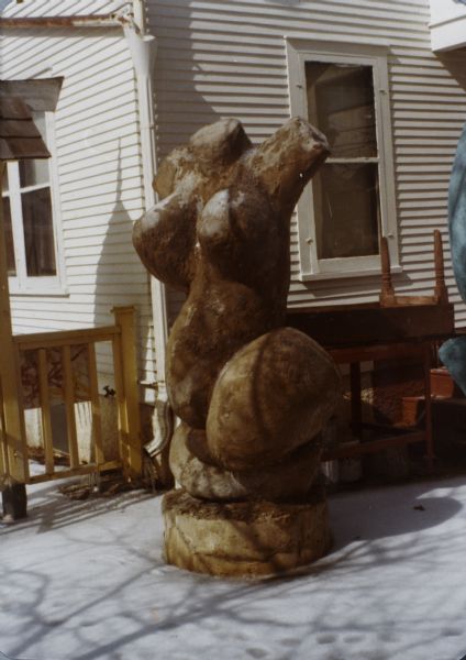 Sculpture of a woman's torso called "Biomorphic Female Abstract in Pink" in Sid's backyard near the side of the house. Snow is on the ground. 