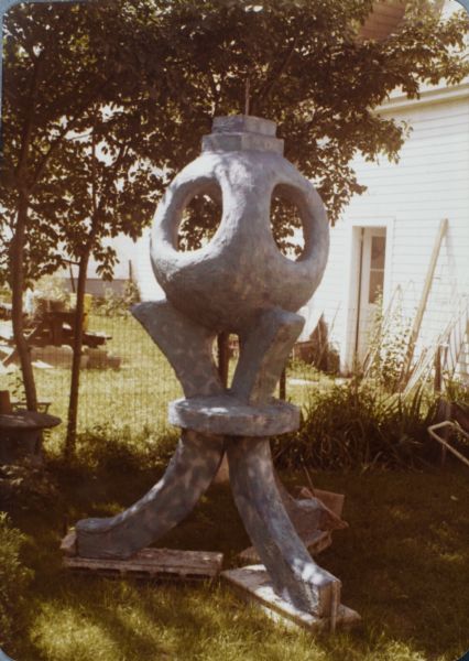 Cast-concrete sculpture identified as "Blue Tripod" in Sid's backyard near a fence. It measures 104" x 31" x 54".