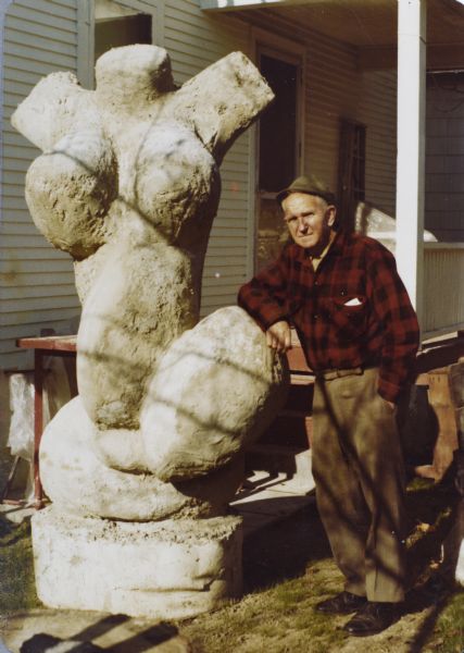 Sid standing next to his sculpture of a woman's torso "Biomorphic Female Abstract in Pink" in his backyard near his porch.
