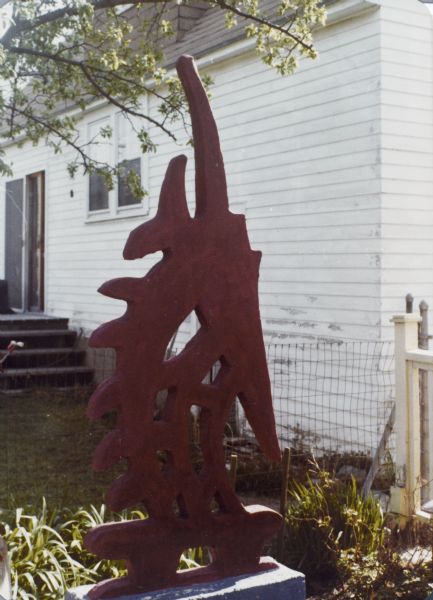 Sid's "African-Influenced Sculpture" in his backyard near the side of a building near a fence. 