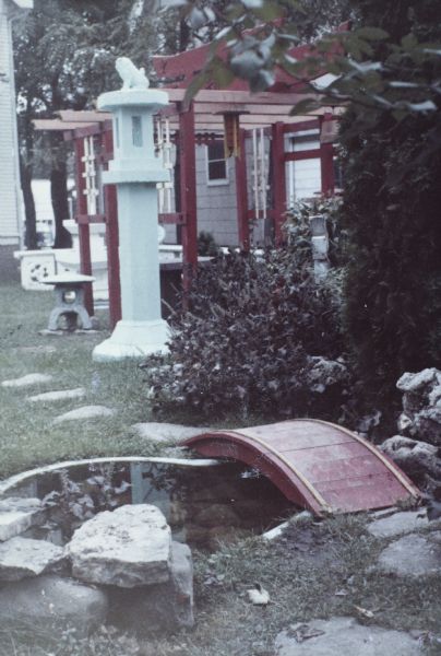 Arched bridge across small pond in Sid's backyard. In the background are a Japanese structure and Fudog lantern.