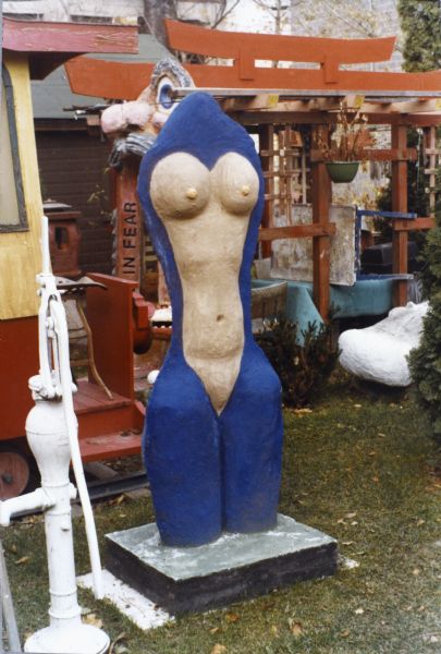 Sculpture "Feminine Torso" in Sid's backyard. There is a hand pump in the foreground on the left.