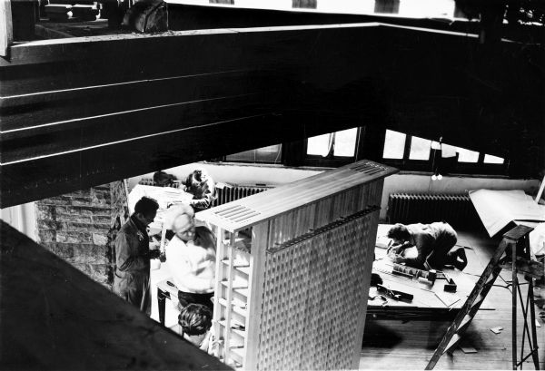 View looking down at Taliesin apprentices rebuilding the Call Tower model first created before 1920. Work is being done in the Hillside Assembly Hall. The Call Tower was intended for a project in San Francisco, but was never built.