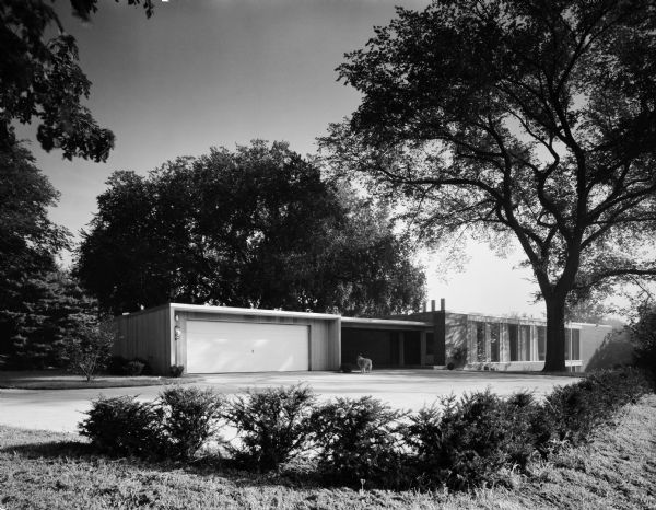 The Donald Buser House was designed by the architectural firm Keck and Keck as Project #573 in 1957. This photograph shows the front of the Buser house in Riverdale, Iowa. A drive through breezeway between the house and garage is shown.