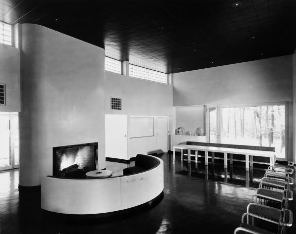 The Bertram and Irma Cahn House was designed by the architectural firm Keck and Keck as Project #213 in 1936. George Fred and William Keck were born in Watertown, Wisconsin, and operated an architectural office on Michigan Avenue in Chicago, Illinois. This photograph shows the living room fireplace, the dining space and the closed bar beyond in the Cahn house on Green Bay Road in Lake Forest, Illinois. Bertram Cahn was President and Chairman of Kuppenheimer Clothing Manufacturers in Chicago. Irma Cahn, after seeing the House of Tomorrow at the Chicago World's Fair (Century of Progress), wanted to have George Fred design her a "House of the Day After Tomorrow."