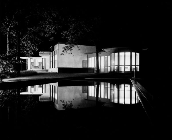The Bertram and Irma Cahn House was designed by the architectural firm Keck and Keck as Project #213 in 1936. This photograph is a night view from the east showing the back of the Cahn house on Green Bay Road in Lake Forest, Illinois, including the swimming pool. Bertram Cahn was President and Chairman of Kuppenheimer Clothing Manufacturers in Chicago. Irma Cahn, after seeing the House of Tomorrow at the Chicago World's Fair (Century of Progress), wanted to have George Fred design her a "House of the Day After Tomorrow."