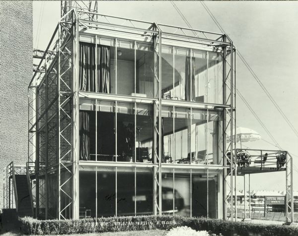 The Crystal House was Keck and Keck Project #183 in 1934. This project was done for the second year of the Chicago World's Fair, named The Century of Progress. The Crystal House was built with glass walls suspended within an external structural steel cage. Fred Keck considered this building a candidate for prefabricated construction and estimated that the house could be built for $3,500 each if production runs would exceed 10,000 units. This exterior photography of the Crystal house shows the silhouette of Buckminster Fuller's Dymaxion three wheeled automobile parked in the garage.