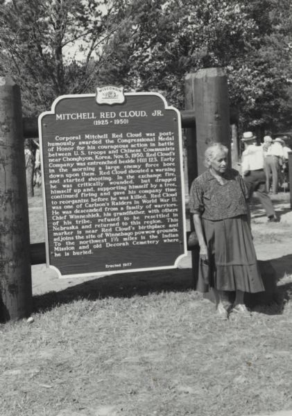 Mrs. Nellie Red Cloud, mother of the Korean War hero, Corporal Mitchell Red Cloud, Jr., standing in front of the historical marker dedicated to her son. She was involved in the ceremony by unveiling the marker to the public and was instrumental in choosing the location for the historical marker. Mrs. Red Cloud selected Jackson County over other possible locations, for it was the birthplace and home of Corporal Red Cloud. 