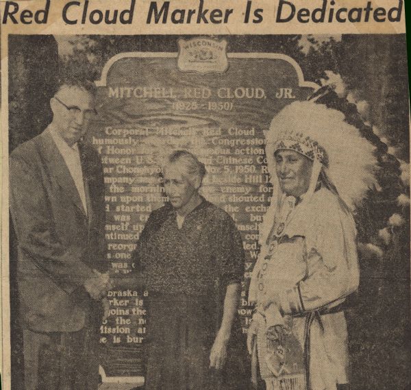 Mrs. Nellie Red Cloud, mother of the Korean War hero, Corporal Mitchell Red Cloud, Jr., shaking hands with V.L. Fiedler, State Highway Commission district engineer at LaCrosse, in front of the historical marker dedicated to her son at Red Cloud Parkway. To her right is standing Chief Daybreak, (Jim Smoke) in full Winnebago regalia. 