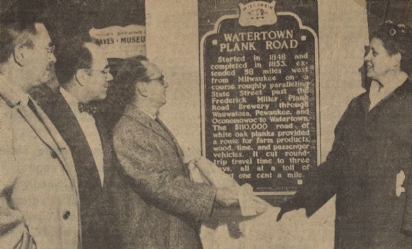 President of the Miller Brewing Company, Norman R. Klug, unveiled the Watertown Plank Road historical marker along with, to his left, James Fitzpatrick, president of the Watertown common council, Frederick I. Olson, president of the Milwaukee Historical Society, and Mrs. Harvey Krebs, on the right. In the background is a sign for the Miller Brewing Co. Caves and Museum.