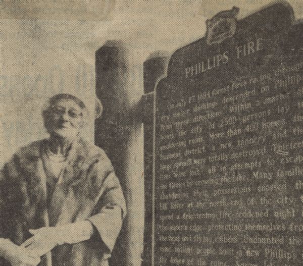 Mrs. James Sima, a child when the Phillips Fire of 1894 raged, standing next to the historical marker documenting the horrific fire.  