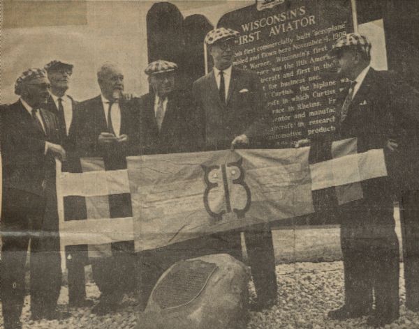 A number of Early Birds of Aviation acquaintances, men who flew solo prior to December 17, 1916, came together to honor A.P. Warner and the historical marker in his honor. From left to right: George Scragg from Cleveland, William Denehie from Chicago, Bert Hassell from Rockford, Jess Brabazon from Beloit, Charles Arens from Winamac, Indiana, and Paul Garber, curator of the National Air Museum, Washington, D.C. The men are holding an Early Bird flag, designed by Mrs. Garber.