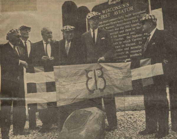 A number of Early Birds of Aviation acquaintances, men who flew solo prior to December 17, 1916, came together to honor A.P. Warner and the historical marker in his honor. From left to right: George Scragg from Cleveland, William Denehie from Chicago, Bert Hassell from Rockford, Jess Brabazon from Beloit, Charles Arens from Winamac, Indiana, and Paul Garber, curator of the National Air Museum, Washington, D.C. The men are holding an Early Bird flag, designed by Mrs. Garber. 