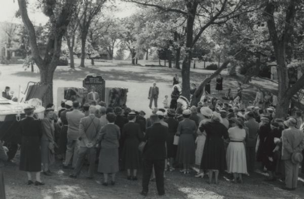 Elevated view over crowd towards speaker during Women's Auxiliary 5th annual pilgrimage to historic sites in Wisconsin. Over 200 members and guests made the journey to Wisconsin Dells and were witness to the dedication ceremony for the Dawn Manor: Site of the Lost City of Newport historical marker. The crowd listens to Clifford L. Lord, Director of the Wisconsin Historical Society, as he dedicates the historical marker. Dawn Manor is in the background, behind the marker.   