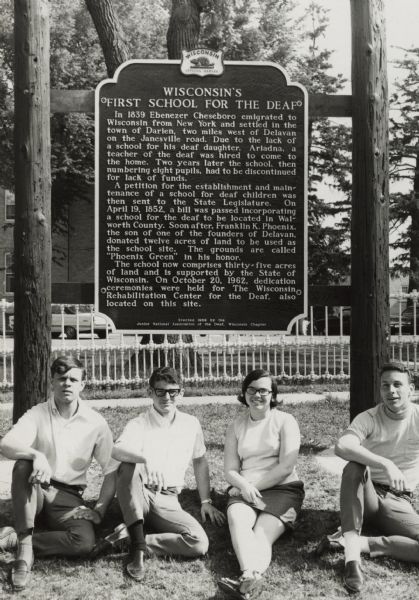 Possibly the officers of the Wisconsin Chapter of the Junior National Association of the Deaf sitting in front of the historical marker documenting Wisconsin's First School for the Deaf in Delavan. This team of officers was primarily responsible for raising the funds necessary to apply for and receive the historical marker. The 1967-1968 officers included: John Harbison, President, Joseph Castronovo, Vice-President, Vonne Gulick, Secretary, and Patrick Cave, Treasurer.