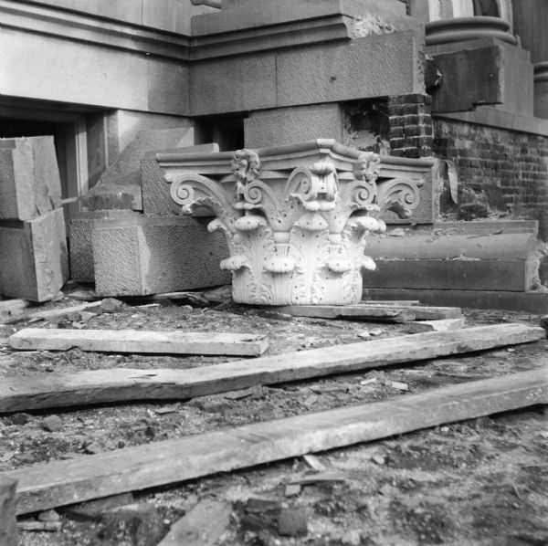 A detailed carved capital awaiting installation is sitting on lumber supports on the ground near the entrance to the Eau Claire Public Library during its construction.