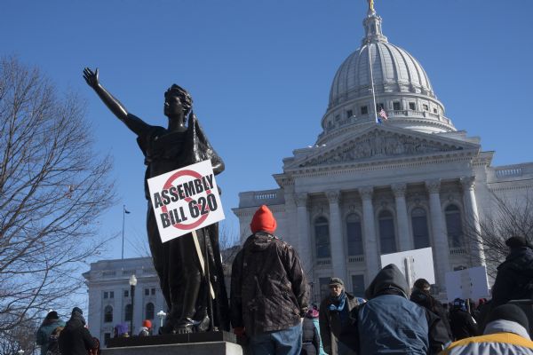Protesters gathering at the Save the Mounds demonstration around the Capitol Square against Assembly Bill 620. A protest sign is attached to the statue "Forward" which reads: "Assembly Bill 620" and has a no symbol (red circle with a slash through it). The Wisconsin State Capitol is in the background.