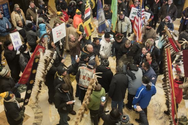 View looking down at the Save the Mounds demonstration on the ground floor of the Wisconsin State Capitol against Assembly Bill 620. In the center is a drum session. Surrounding the drummers are demonstrators holding flags, standards and signs.