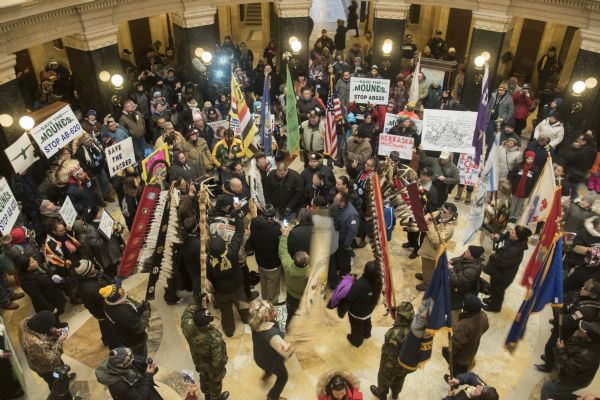 View looking down at the Save the Mounds demonstration on the ground floor of the Wisconsin State Capitol against Assembly Bill 620. In the center is a drum circle. Surrounding the drummers are demonstrators holding, flag, standards and signs.