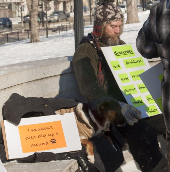 A demonstrator sits with his dog during the Save the Mounds demonstration around the Capitol Square against Assembly Bill 620. He is holding a sign explaining the word "desecrate," and his dog has a sign that reads: "I wouldn't even dig up a mound."