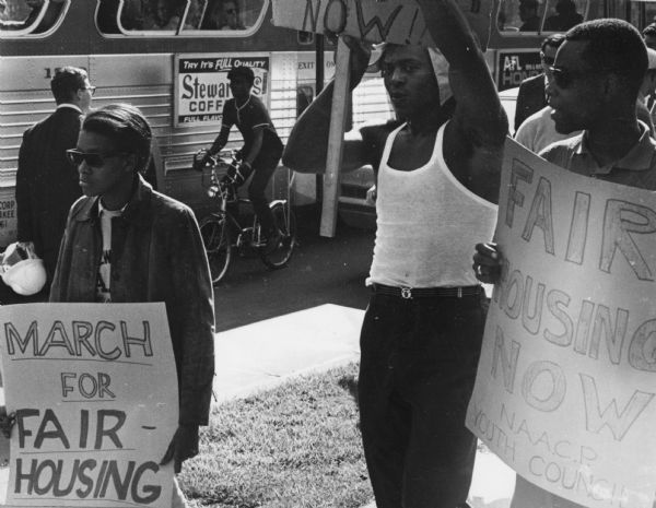 Men and women walking along a sidewalk carrying Fair Housing signs. The bottom of one sign reads: "NAACP Youth Council."