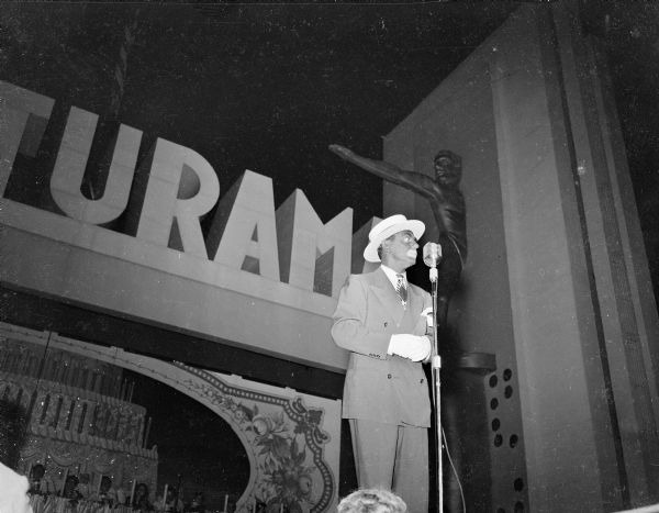 Eddie Cantor, in blackface, standing on stage at Centurama in front of a microphone.