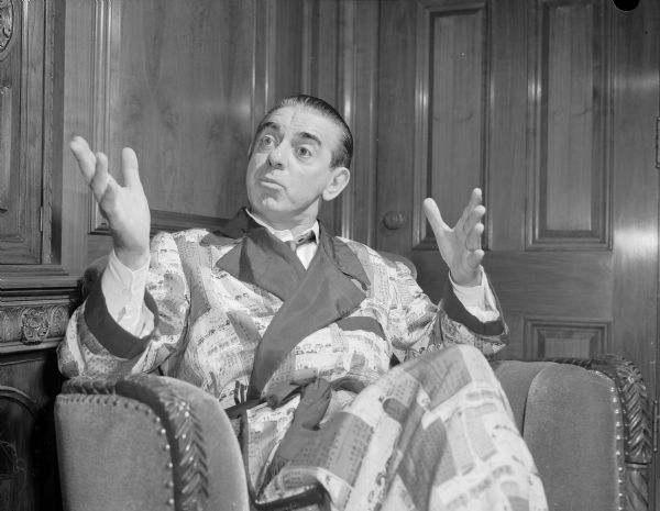 Eddie Cantor, sitting in a chair wearing a robe and gesturing with his hands.