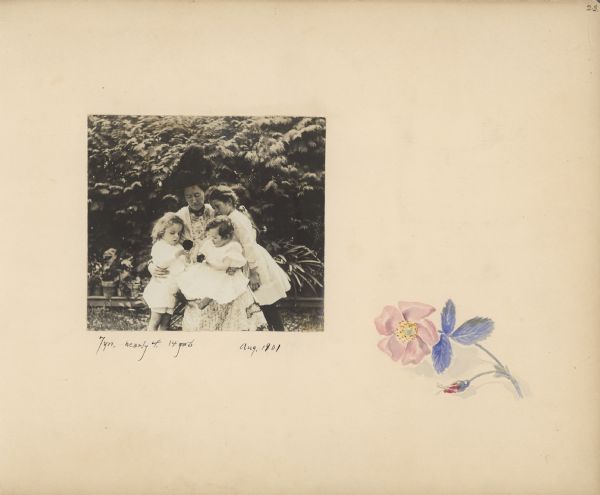 A photograph of Louise Mears Fargo and her children is mounted on an album page decorated with a hand-painted wild rose. In the photograph, Louise, wearing a large plumed hat, is sitting outdoors holding her son Frank, age 14 months. Daughter Dorothy, age 7 years, is standing on the right; Stuart, age "nearly 4," is on the left. The boys are each holding a flower. There are potted plants on a low shelf behind them.