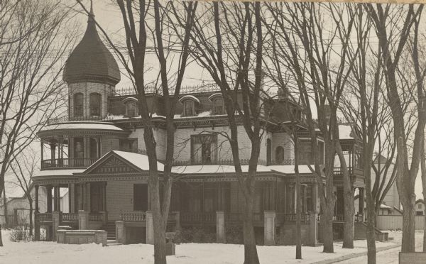 A winter view of the front of the Fargo house on Mulberry Street. It is a two and one-half story cream brick Second Empire Style house with mansard roof. There is decorative ironwork on the roof of the house and also on the porches. A polygonal tower with onion dome in on the left. A two-story porch wraps around the tower and extends as a single story across the front and down the right side.